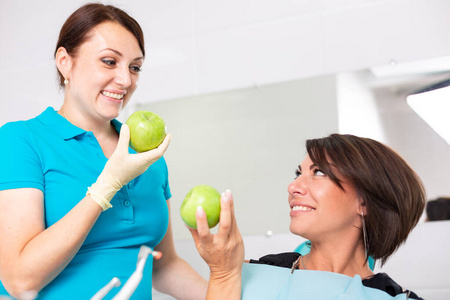 一个快乐的病人在雄蕊学家的接待处，检查牙齿的健康状况，咬青苹果。牙科理念，健康的牙齿，美丽的笑容。