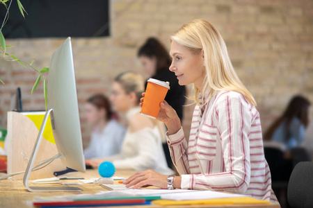 一个金发女人在电脑前工作，喝着咖啡