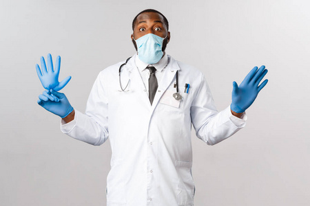 Covid19，冠状病毒患者治疗和疾病概念。滑稽的非洲裔男性医生戴上口罩，防止病毒爆发，与小孩玩耍，吹拂乳胶手套。