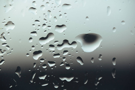 巨大的纯雨滴落在玻璃上，背景是云灰色