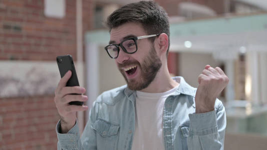 戴着眼镜的快乐年轻人在智能手机上庆祝