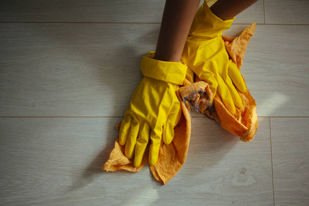 检疫期间打扫房子。女孩用黄色的布把脏兮兮的地板洗干净，戴着黄色的防护手套