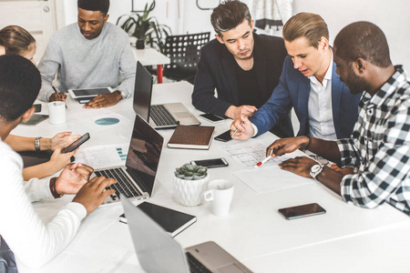 群年轻的上班族,拿着笔记本电脑在桌旁工作的商人,在办公室里一起交流