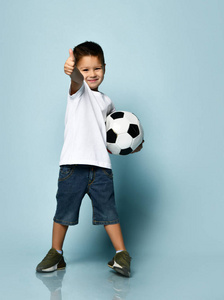 微笑,伸出大拇指,举着足球,在蓝色背景上摆姿势照片