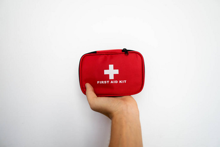 手拿着一个红色的急救箱，背景是白色的墙。