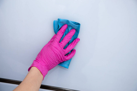 手戴粉红色手套，用蓝色超细纤维布擦拭白色光滑表面。打扫房间。