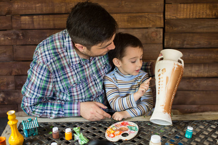 父子俩靠着木墙画花瓶。