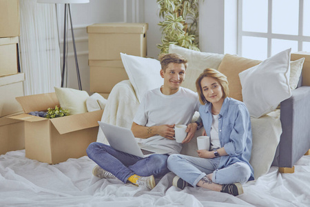 幸福夫妇坐在新房子里，围着盒子看着笔记本电脑
