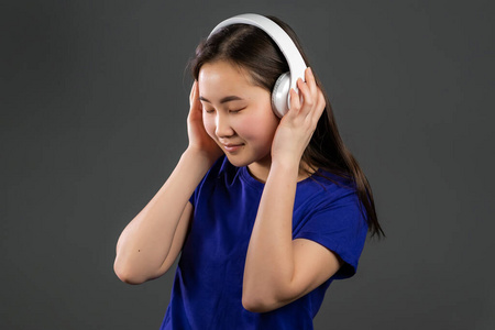 年轻美丽的亚洲女子戴着耳机，戴着现代服装，在灰色背景下尽情跳舞。收音机，旋律，技术概念。
