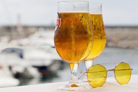 在港口的码头和游艇的背景上放着两杯冰镇啤酒和墨镜。