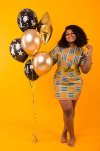 假日，生日聚会和有趣的概念微笑的年轻非洲裔美国年轻女子画像看起来甜美的黄色背景下手持气球。