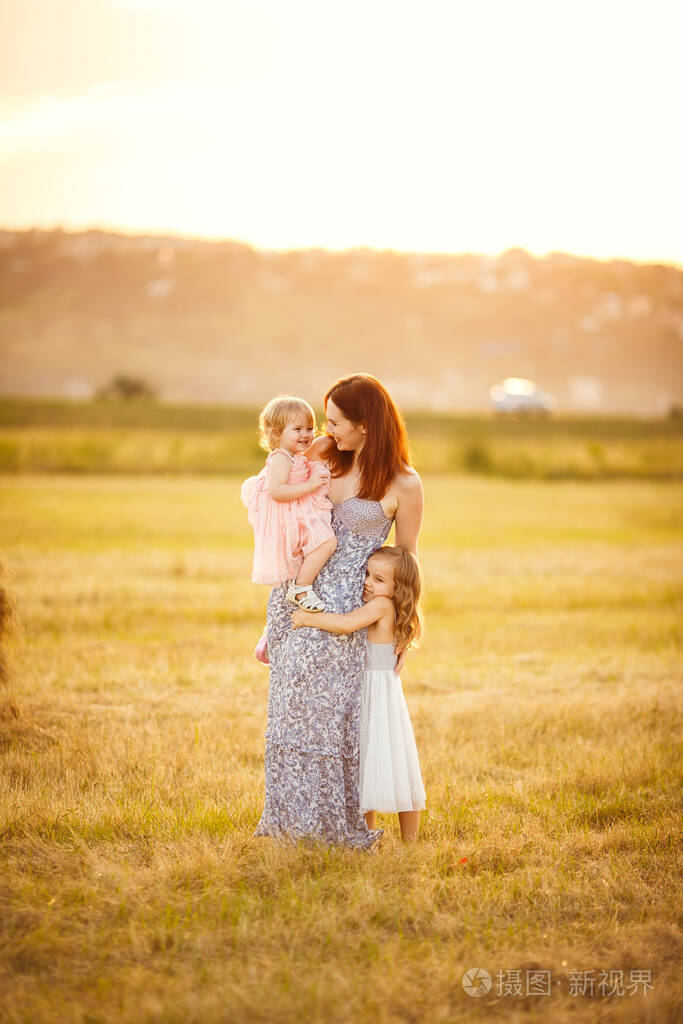 妈妈和两个女儿站在一起拥抱修剪过的田地