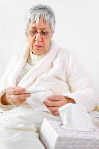 冠状病毒。生病的老年妇女拿着纸巾和体温计坐在床上，心烦意乱的老太太感冒了，独自在家得了冠状病毒流感症状。