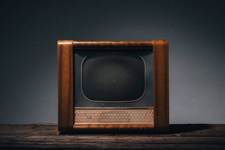 20世纪60年代的老式木制电视机,在灰色背景下的木桌上照片