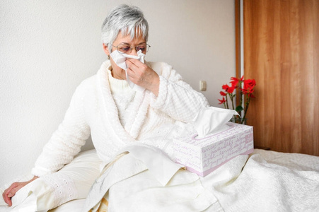 冠状病毒大流行。医疗保健，流感，卫生和人的观念。生病的老太太在家里用纸巾擦鼻涕。