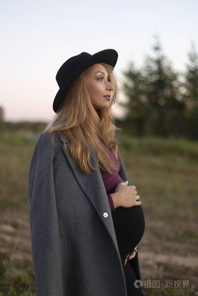 平静美丽的孕妇抱着肚子憧憬着户外