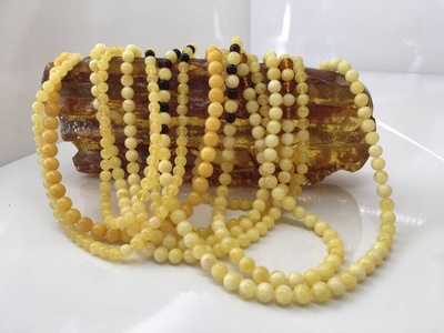 A lot of Baltic amber white beads lie on a piece amber. 