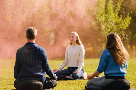 A group of young people meditate outdoors in a park. 