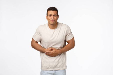 帅哥心烦意乱的年轻人觉得肚子不舒服,摸着肚子像在受胃痛,弯腰,做