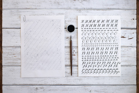木制背景上的书法纸笔尖纸墨水。用画笔书写的英语字母表中的字母。