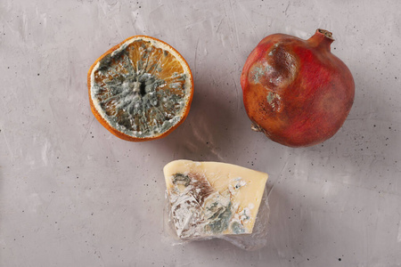 腐烂变质的发霉食物:半个橘子,石榴和硬奶酪,灰色背景,俯视图照片