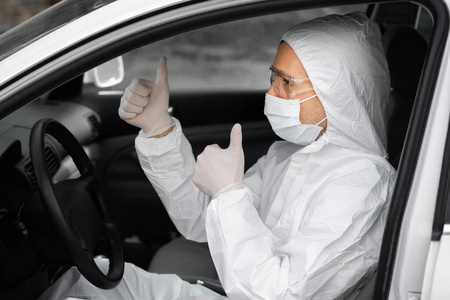 穿着防护服医用面罩和橡胶手套的男子坐在车里，竖起大拇指。检疫，世界大流行，covid19，冠状病毒，感染。