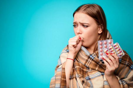 感染病毒的妇女咳嗽，手里拿着用格子布包着的药片。蓝色背景
