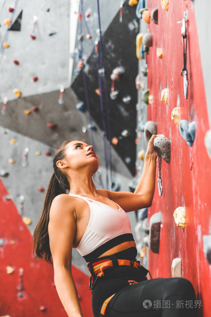 女运动员爬上陡峭的岩石爬上室内的人造墙极限运动与抱石概念