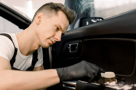 专业洗车服务人员戴着黑色防护手套，用特殊的化学泡沫和软刷清洁汽车内部。选择性关注工人脸