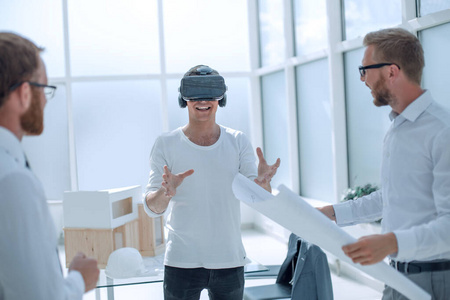 戴着虚拟现实头盔的年轻设计师站在建筑办公室里