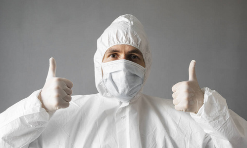 身穿白色防护服医用面罩和橡胶手套的医生伸出大拇指。在冠状病毒大流行威胁下帮助人们。流行，冠状病毒covid19大流行。