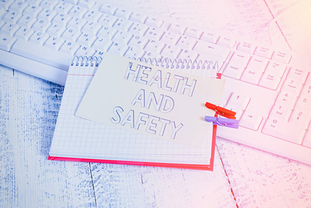 显示健康和安全的文字标志。概念照片程序旨在防止工作场所事故笔记本纸提醒衣夹别针床单白色键盘轻木。