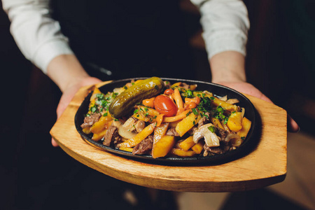 餐馆服务员手里的煎锅里的蔬菜和热肉。