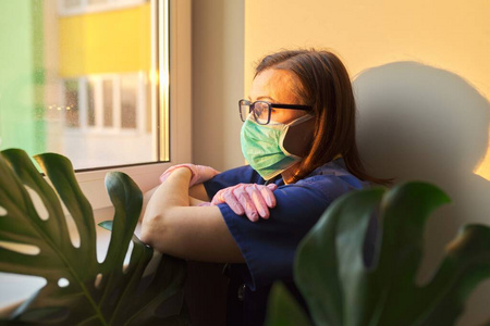 医生妇女戴着医用面罩望着诊所的窗户