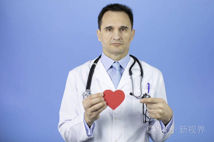 蓝色背景的医生手里拿着心脏用食指指着它