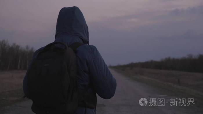 一名男子背着一个带着防护面罩和面罩的背包离开了城市沿着公路走在