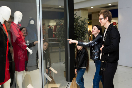 快乐的年轻一家带着纸袋在商场购物.在橱窗里买衣服.照片