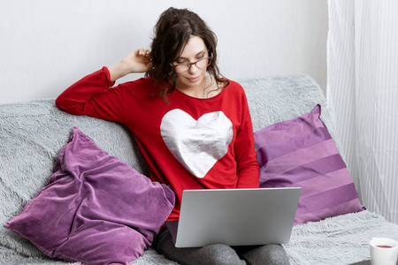 女人躺在沙发上看着笔记本电脑.在家休息的女孩照片