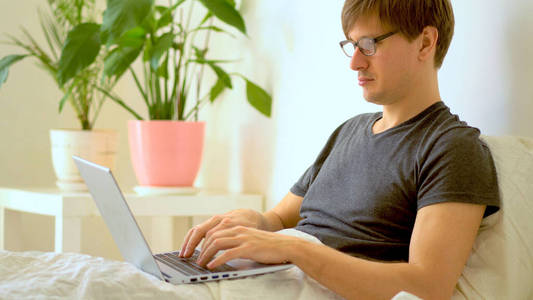 一个戴眼镜的男人在卧室里用笔记本电脑工作。