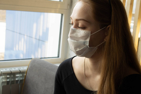 Beautiful girl sits and works at the table in a medical mask. On