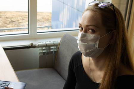 Beautiful girl sits and works at the table in a medical mask. On