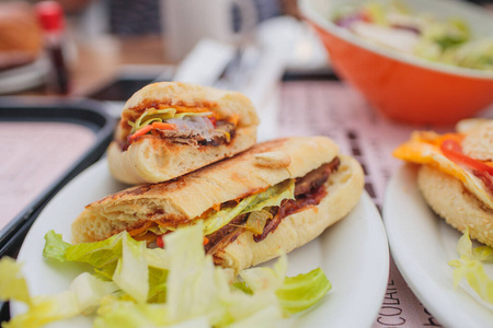牛角面包三明治，火腿，奶酪和西红柿放在木制的砧板上。黑色的木制桌子后面有白色的纸咖啡杯。