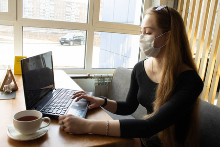 Beautiful girl sits and works at the table in a medical mask. On