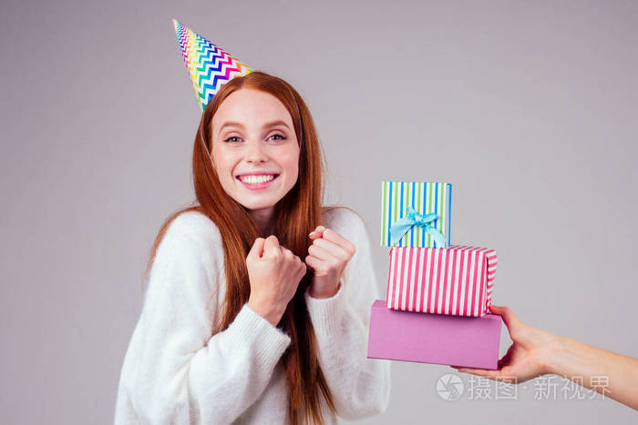 红发姜黄色女人戴着生日帽喇叭拿着许多礼品盒在工作室白色背景