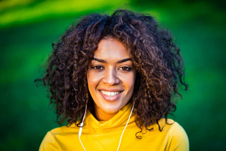 戴着白色耳机的美国黑人女孩的肖像。一个黄色卷发的年轻女子在公园里欣赏音乐。