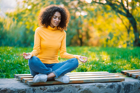 Young beautiful african american woman meditating at city park, 