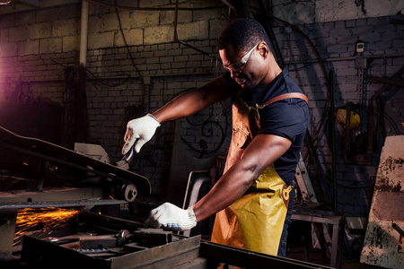 铁男英俊的非洲裔美国铁匠男工人,穿着皮围裙在车间工作照片