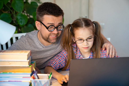 戴眼镜的爸爸用笔记本电脑帮女儿上课