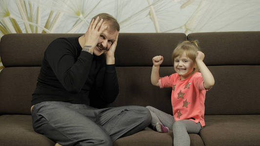 爸爸和小女儿笑着，一起在沙发上玩。休闲游戏