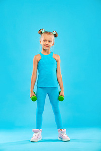 小女孩做健身或瑜伽练习，哑铃被隔离在蓝色背景上